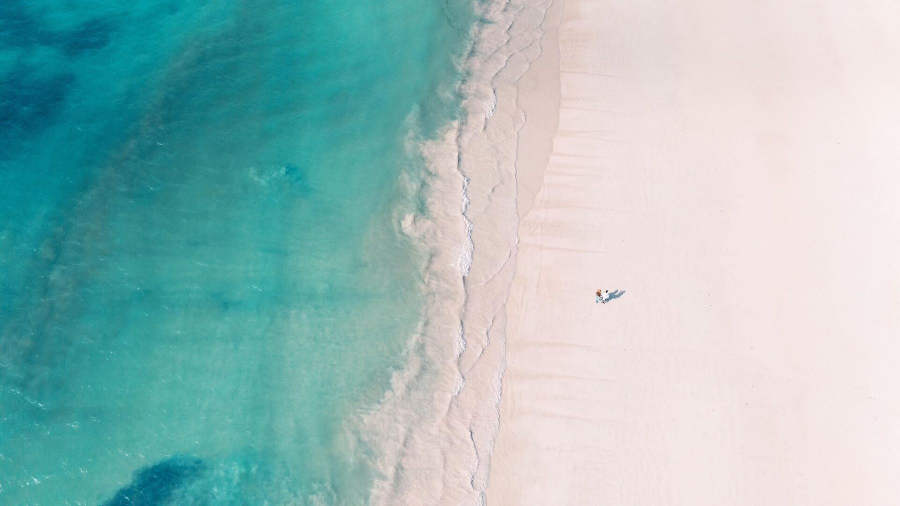 Aerial view of white sand meeting turquoise water on Galu Beach, with a single figure on the beach