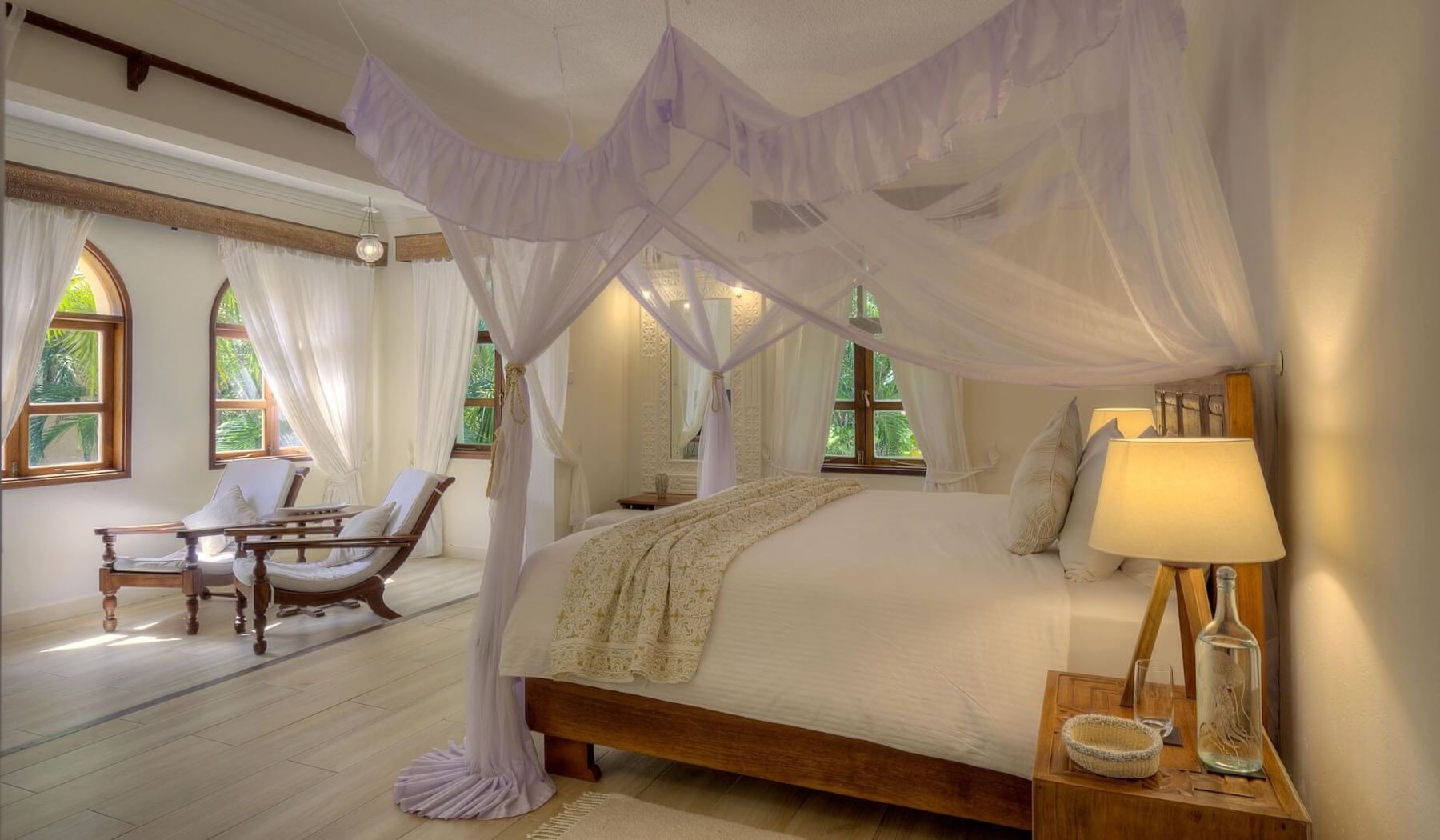 Villa bedroom at Almanara with a draped canopy bed, arched windows and two reclining chairs