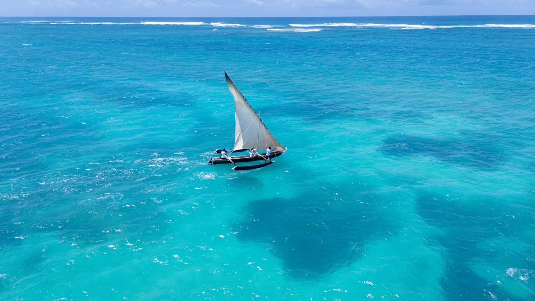 A traditional dhow sailing over clear turquoise water and coral reef off Diani