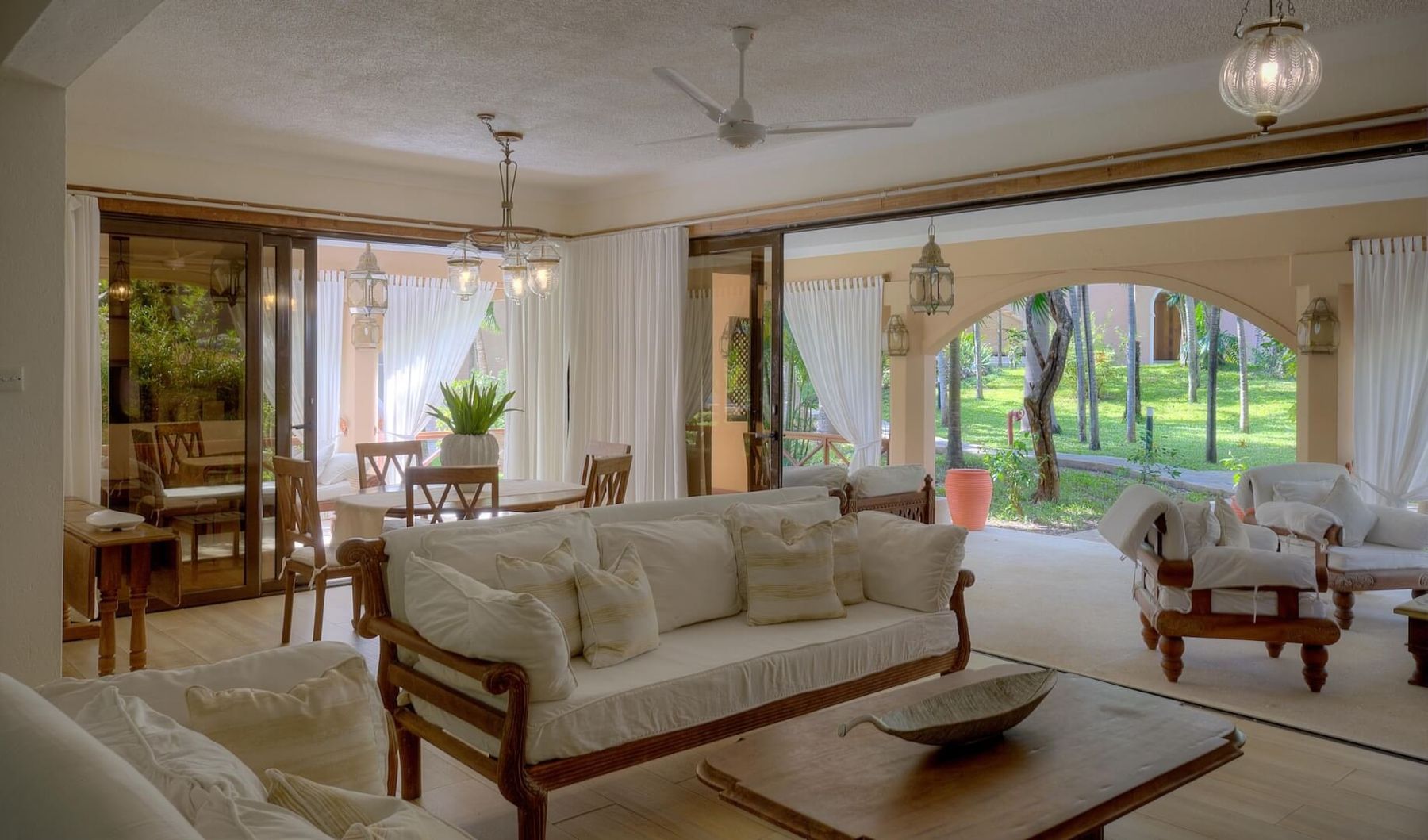Living room of a villa at Almanara with white sofas, carved wooden furniture and arches opening onto the garden
