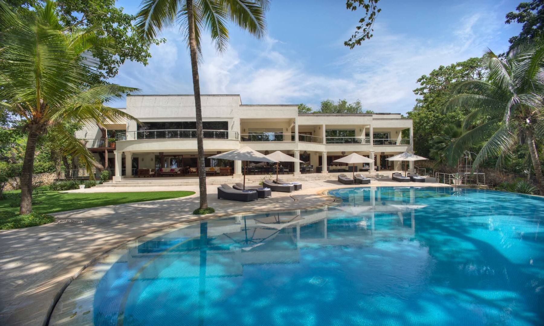 The large lagoon pool at Almanara, with loungers and umbrellas in front of a white building among palms