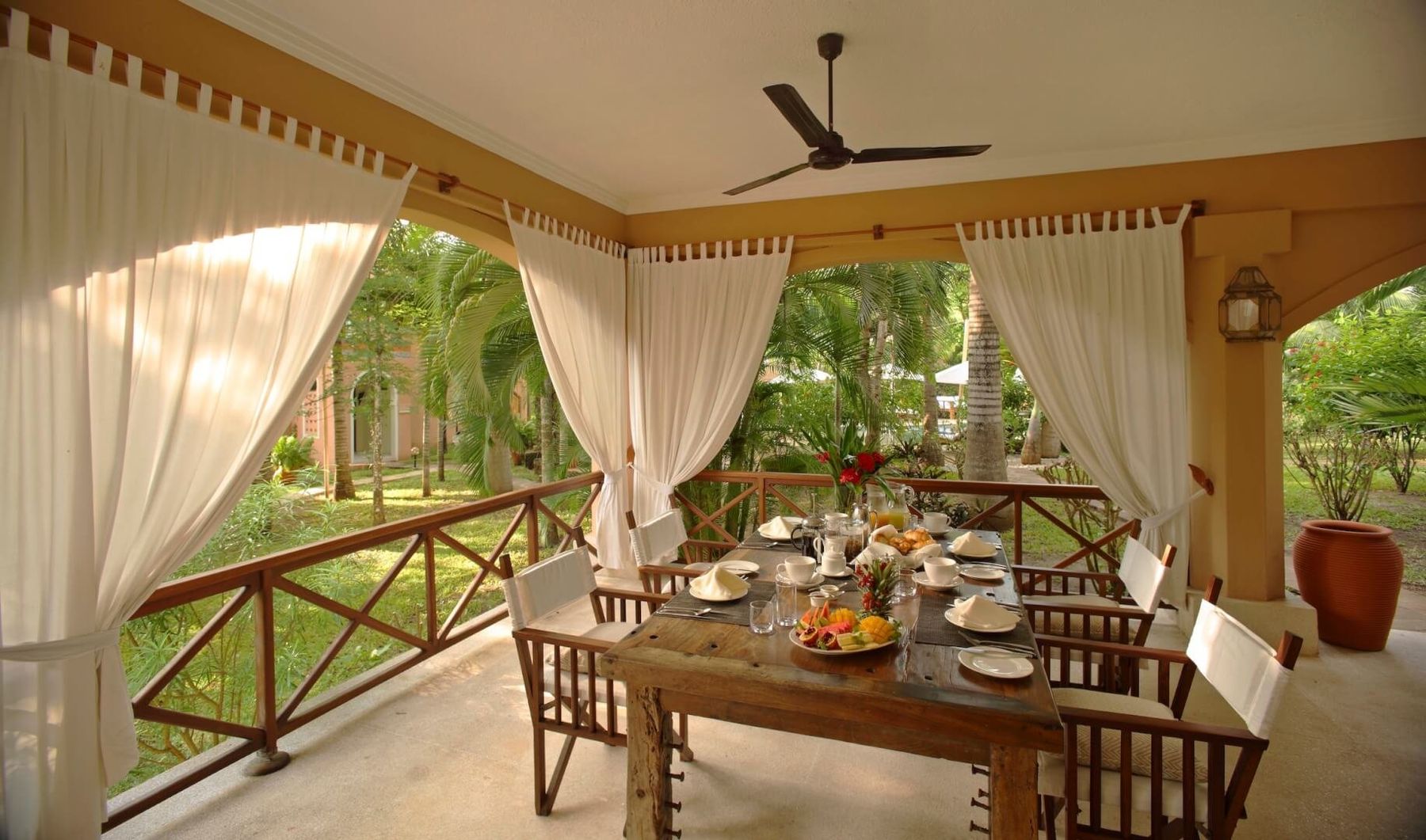 A breakfast table laid on a curtained villa veranda at Almanara, overlooking the garden
