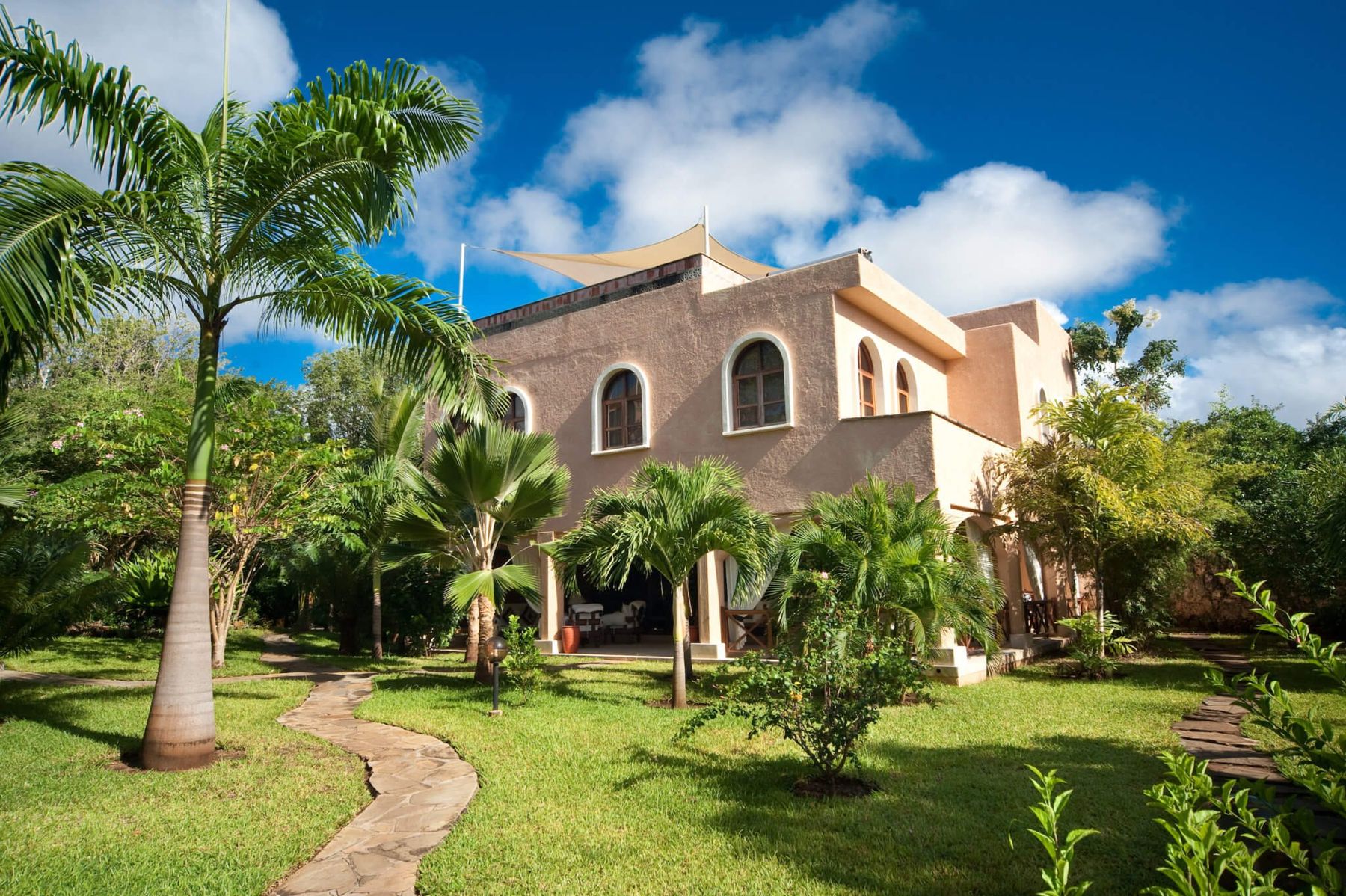 A two-storey villa at Almanara with arched windows and a sail-shaded roof terrace, among palms and lawns