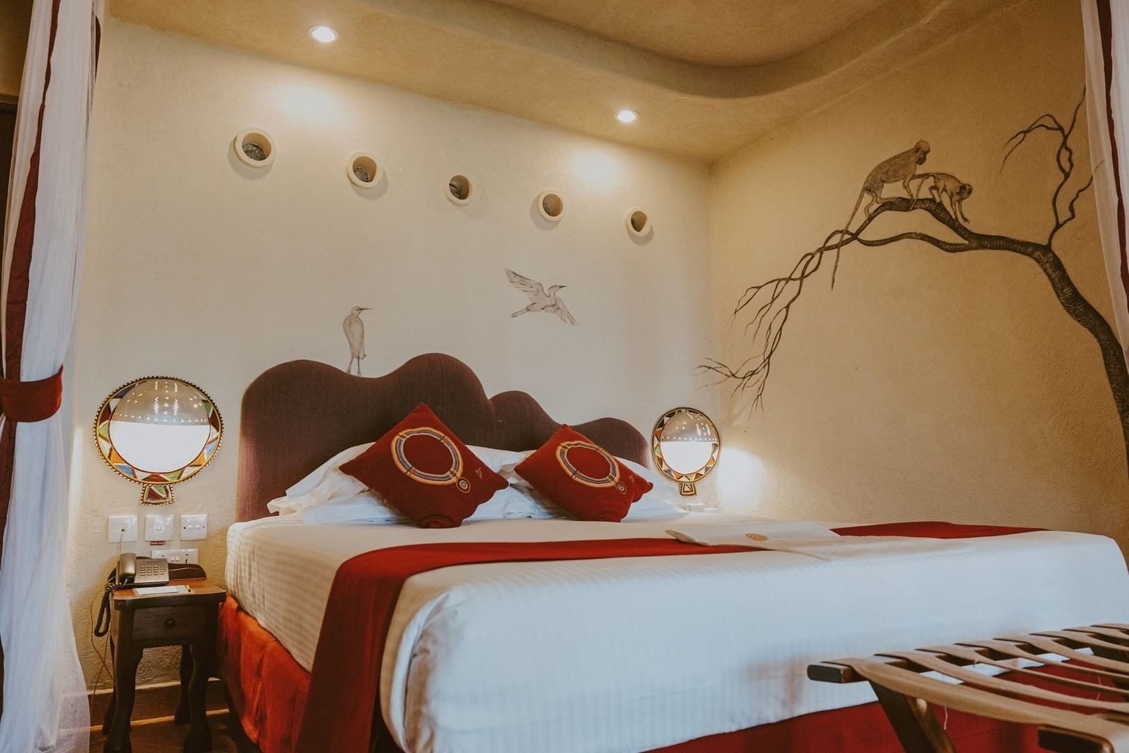Double room at Amboseli Serena Safari Lodge with red cushions, a curved headboard and birds painted on the cream walls