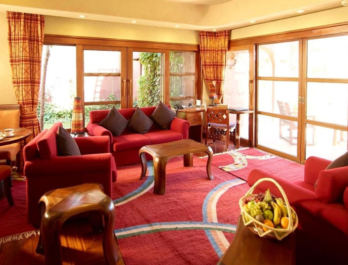 Bright suite sitting room at Amboseli Serena Safari Lodge with red sofas, a carved coffee table and tall windows