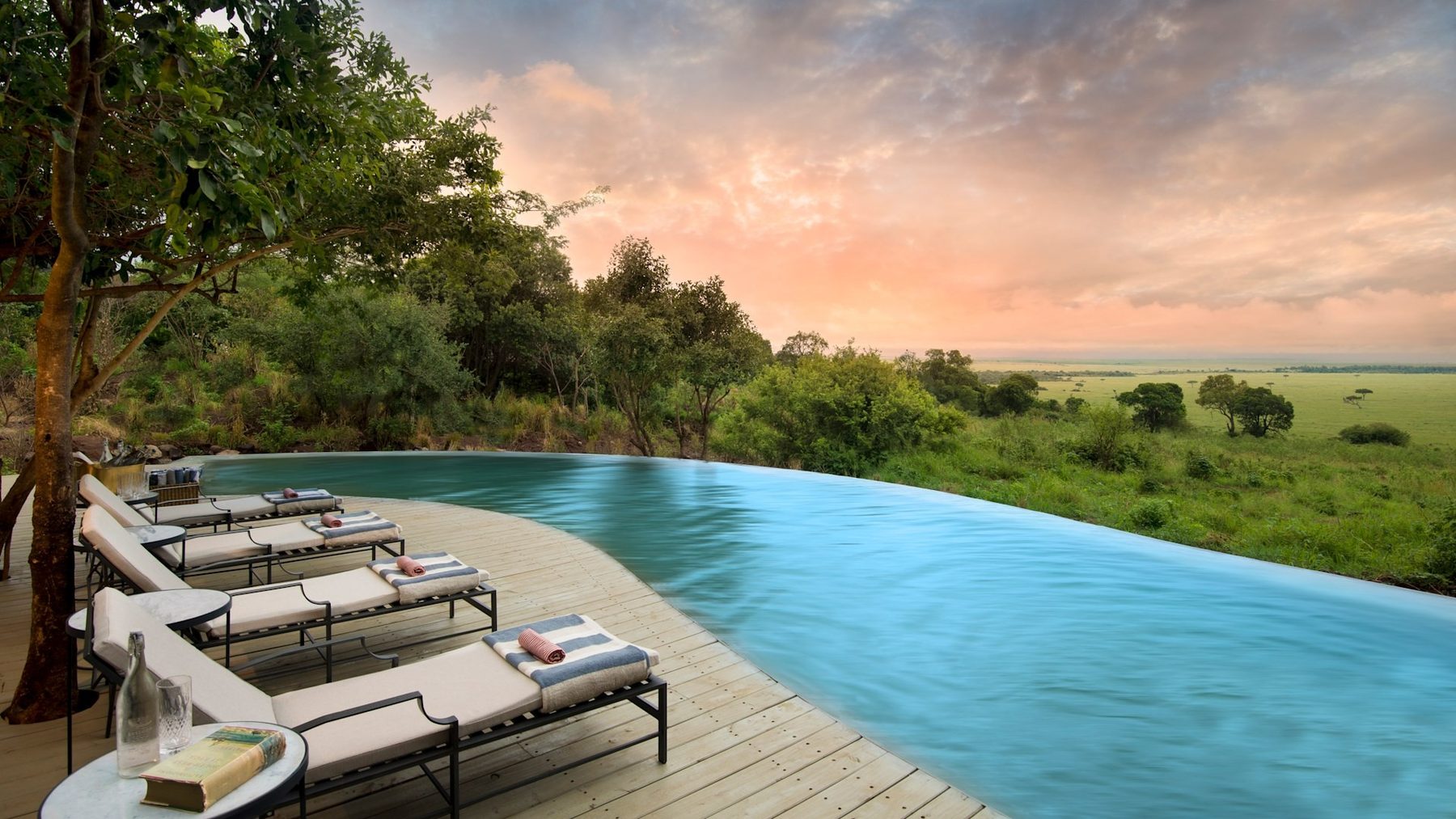 Infinity pool with loungers on a wooden deck at &Beyond Bateleur Camp, looking out over bush and grassland