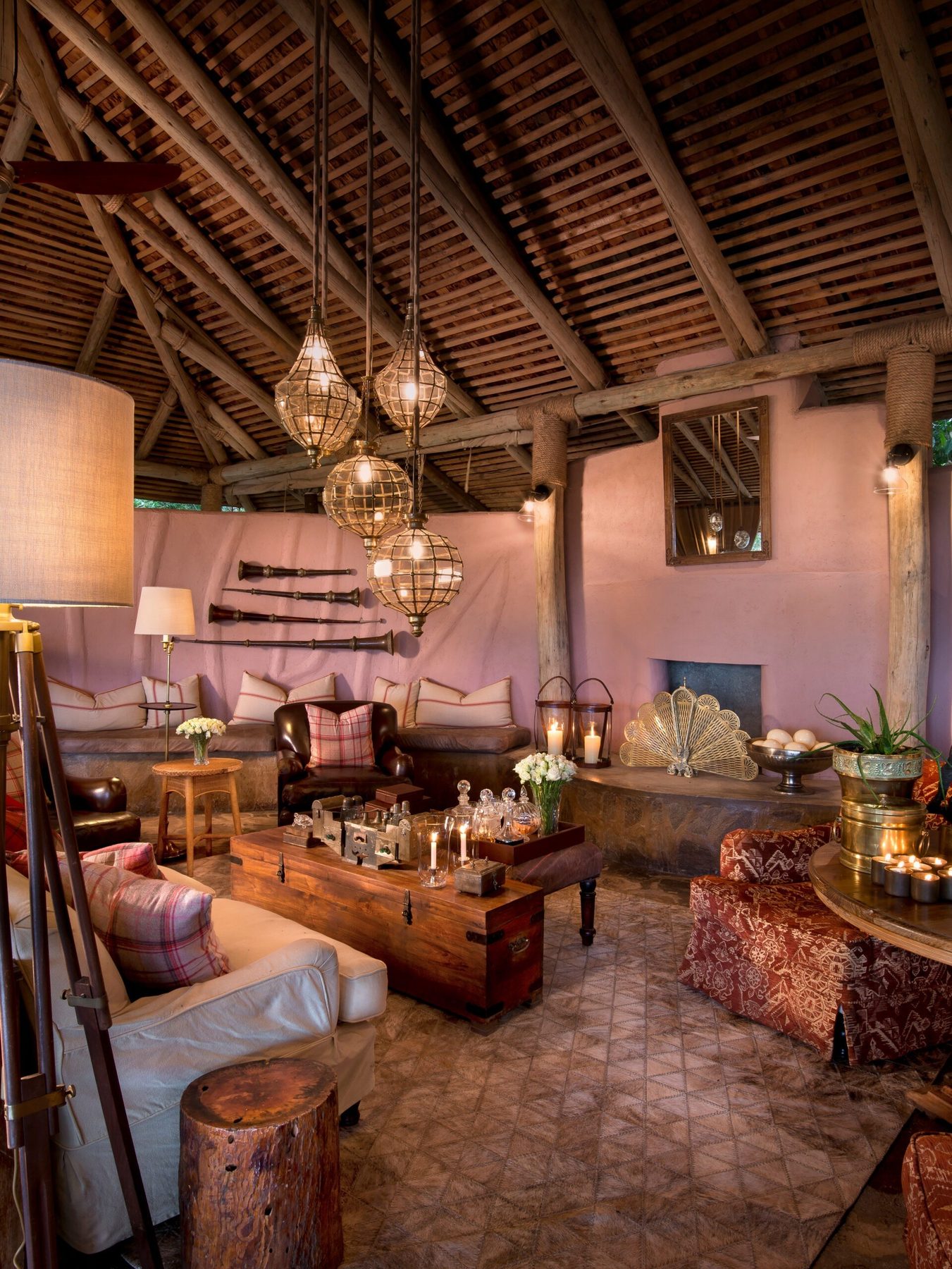 Main lounge at &Beyond Bateleur Camp under a timber roof, with hanging lanterns, sofas, rugs and a fireplace