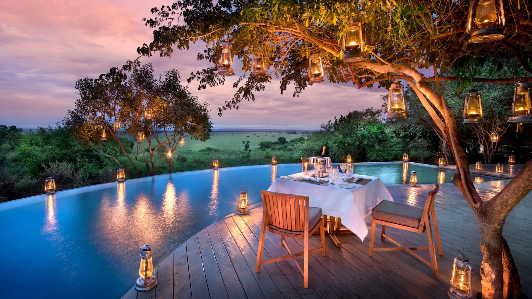 Table for two on the pool deck under a tree hung with lanterns at &Beyond Bateleur Camp at dusk