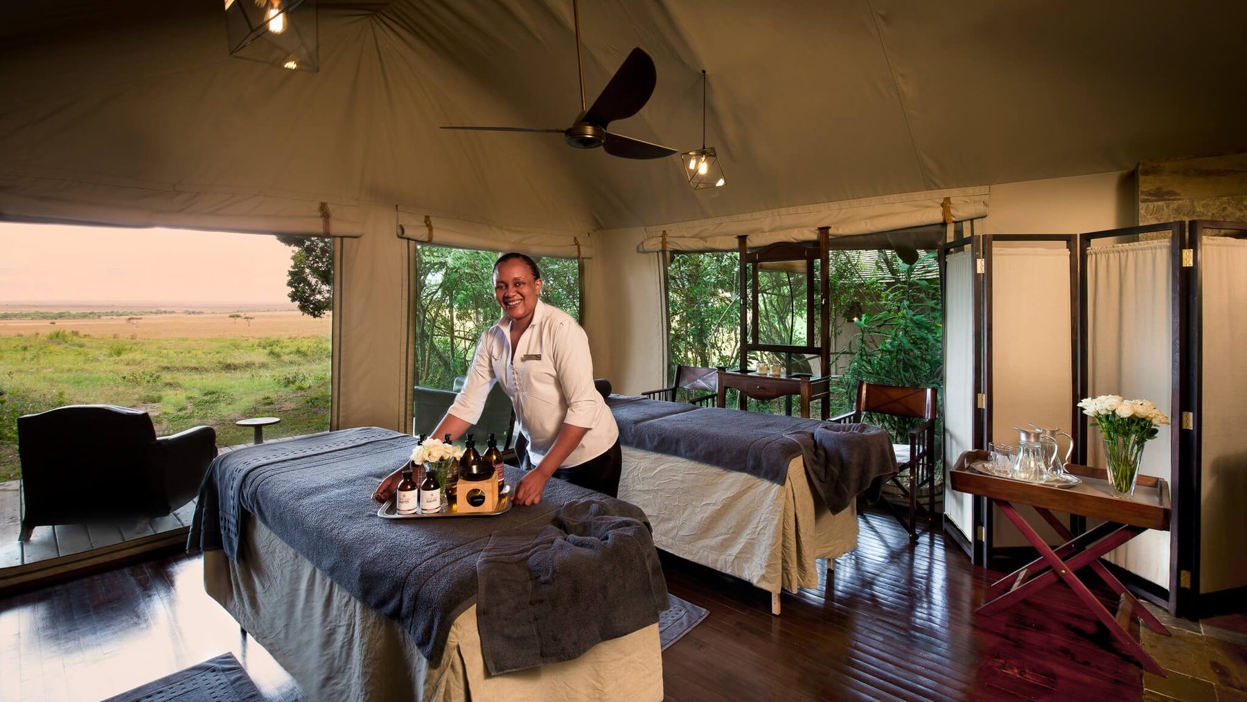 Spa tent at &Beyond Bateleur Camp with two massage beds, a therapist laying out oils and windows onto the bush