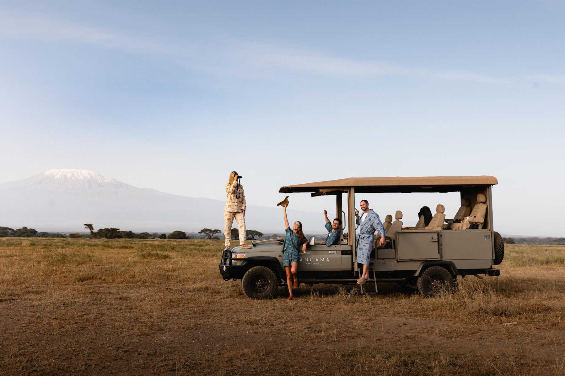 Open game drive vehicle on dry grassland near Angama Amboseli, with guests standing and Kilimanjaro behind