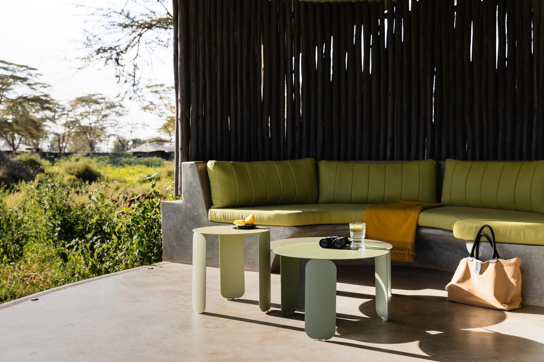 Green cushioned sofa and low tables on a shaded terrace at Angama Amboseli, looking out to the bush