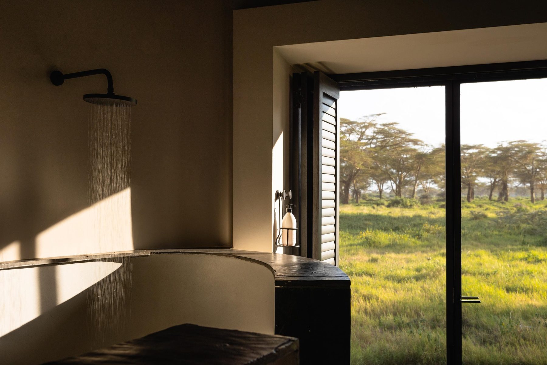 Bathroom at Angama Amboseli with a rain shower and tall windows framing fever trees and grassland