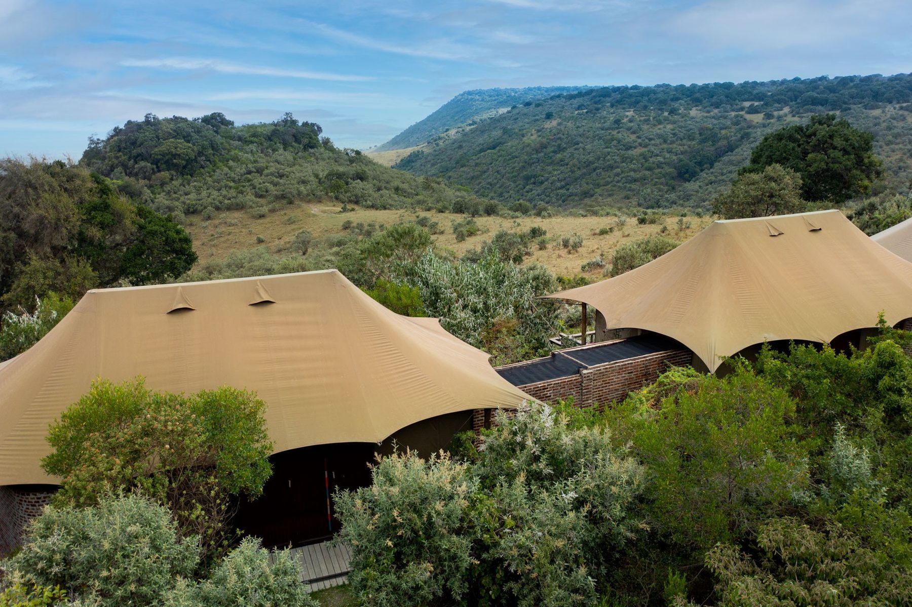 Canvas-roofed tents among green bush on the escarpment at Angama Mara, with a long valley stretching beyond