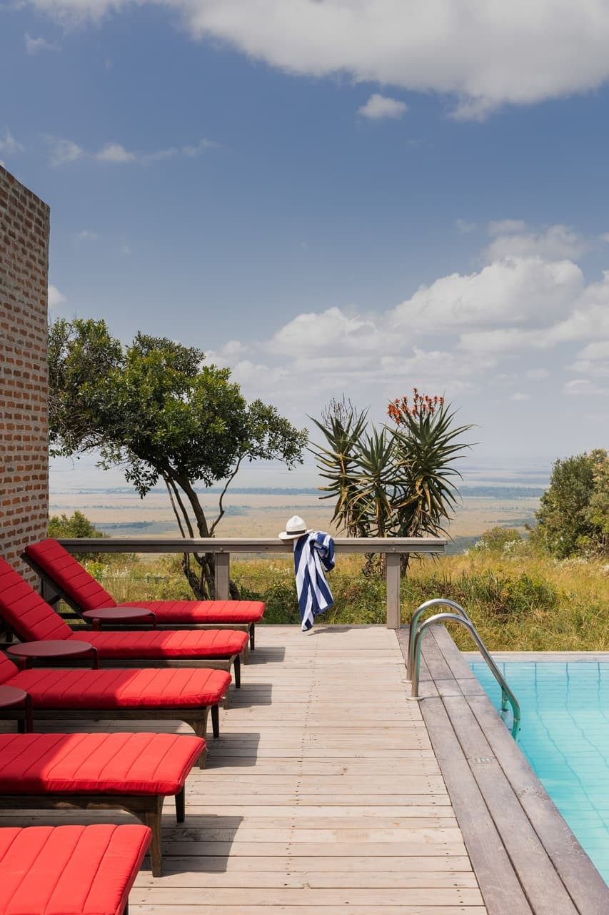Red sun loungers on a wooden deck beside the pool at Angama Mara, with trees and open sky beyond