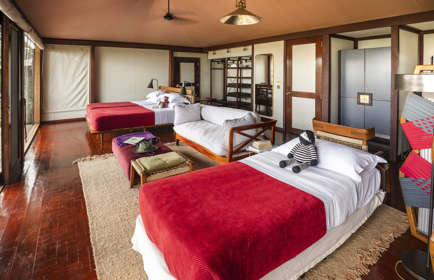 Twin beds with red blankets, a safari hat and a striped toy zebra in a tented room at Angama Mara