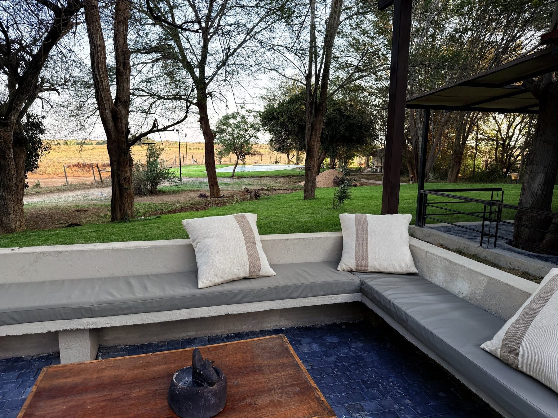 Sunken outdoor seating with white cushions and a low wooden table at Ashnil Aruba Lodge, looking over the lawn
