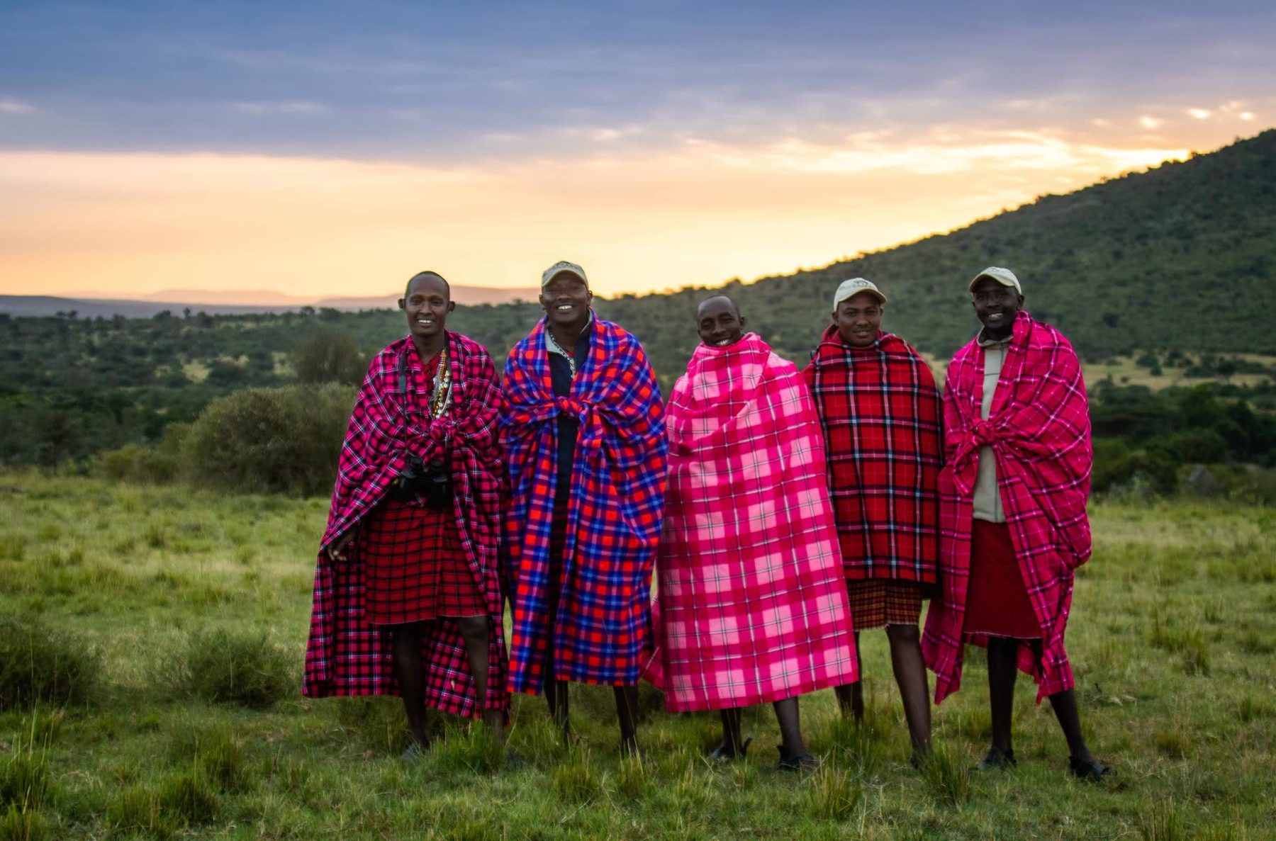 Five Maasai men in red and pink shukas on grassland near Cottar’s 1920s Camp at sunset