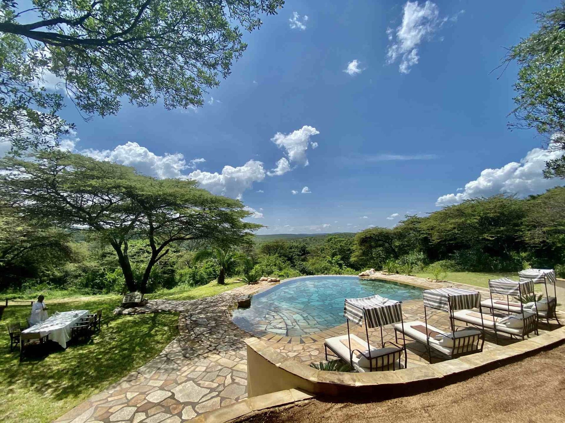 Pool with loungers on a stone terrace at Cottar’s 1920s Camp, overlooking acacia trees and hills