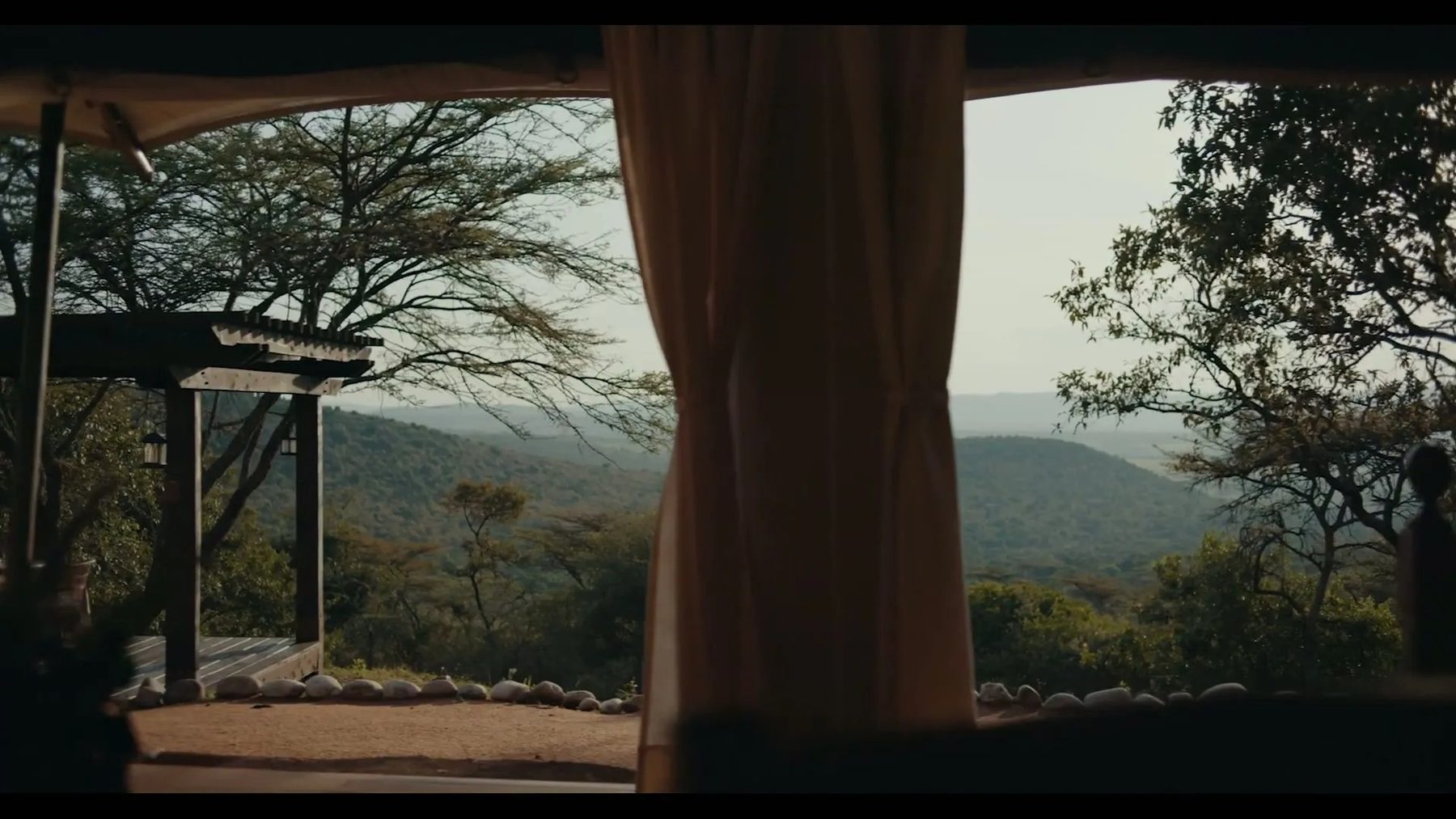 Curtain drawn back from a tent at Cottar’s 1920s Camp, framing a view over wooded hills