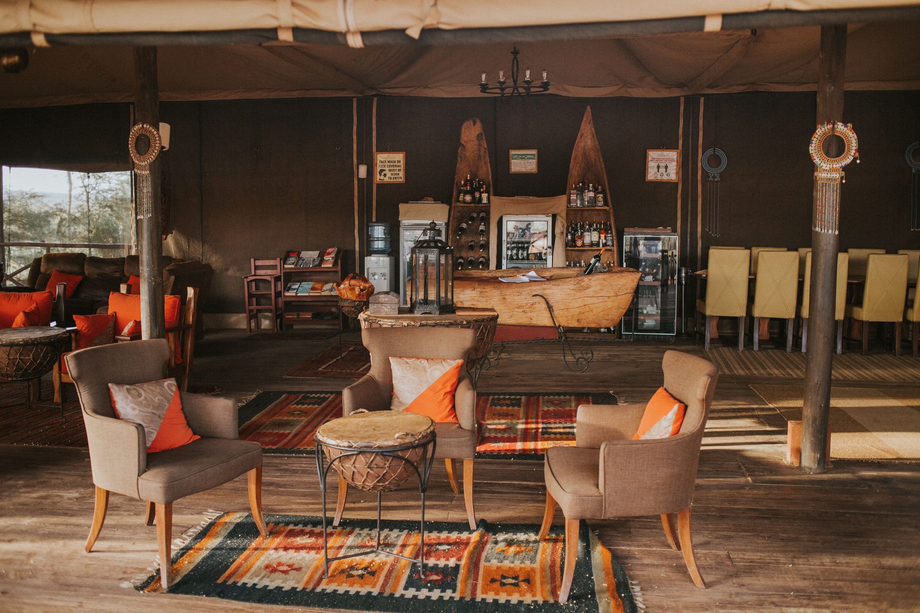 Main tented lounge at Elephant Bedroom Camp with armchairs, orange cushions, patterned rugs and a bar behind