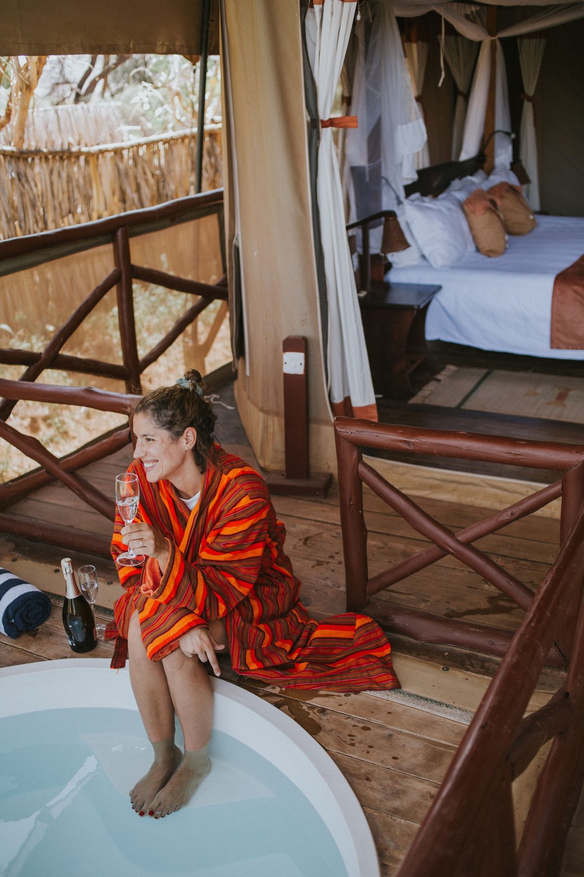Guest in a red robe sitting at the edge of a plunge pool on a tent deck at Elephant Bedroom Camp