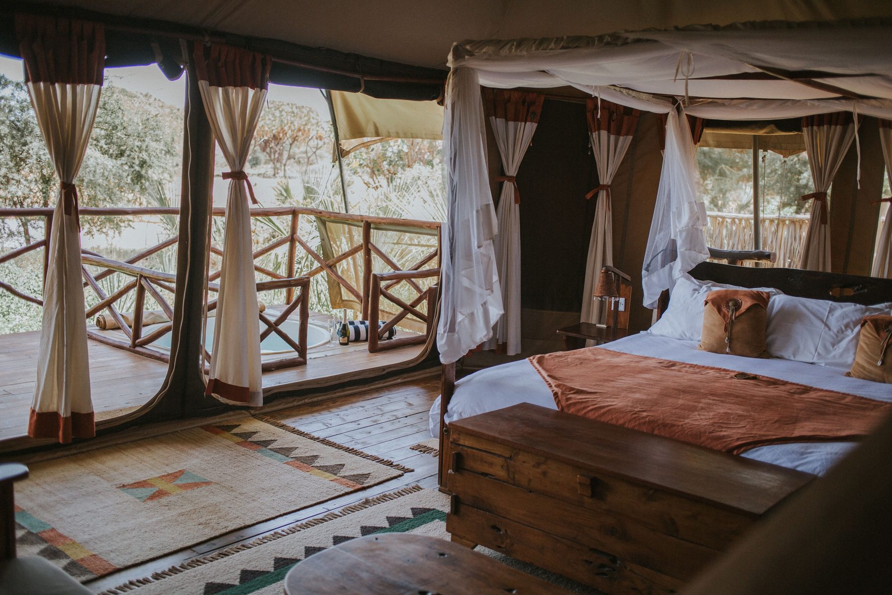 Bed with an orange throw and a wooden chest inside a tent at Elephant Bedroom Camp, curtains open to the deck