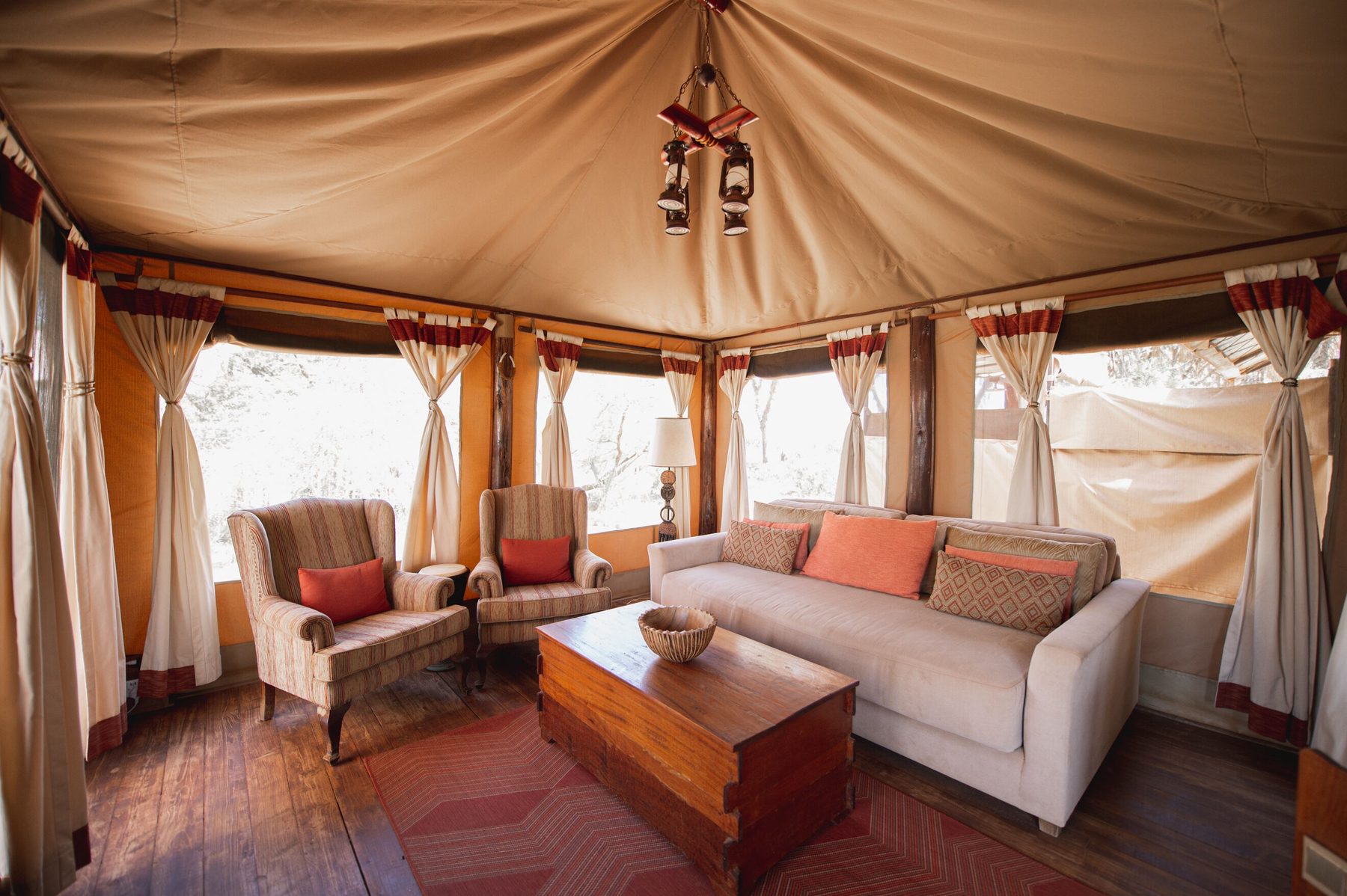 Sitting area inside a tent at Elephant Bedroom Camp with a cream sofa, armchairs and windows on three sides