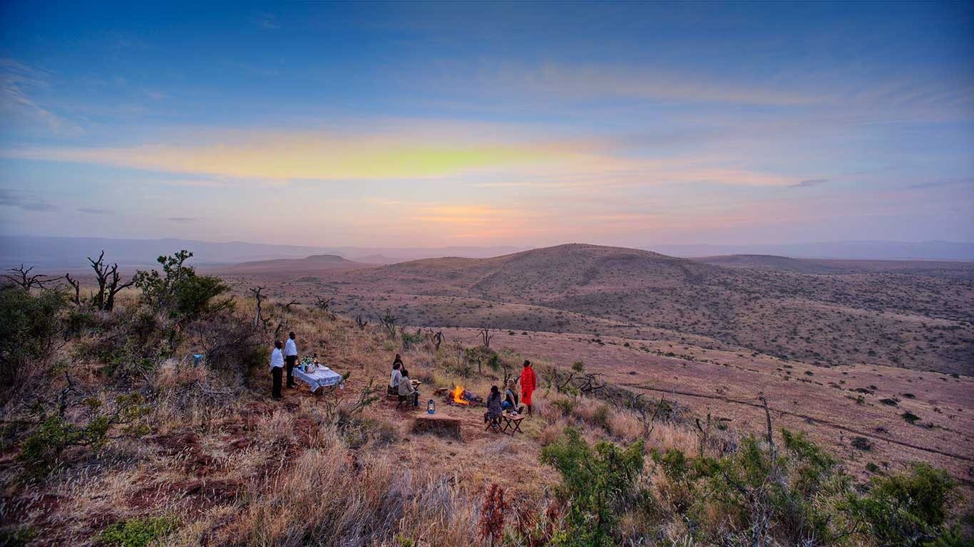 Guests gathered for sundowners on a hilltop overlooking rolling bush country on Lewa at dusk