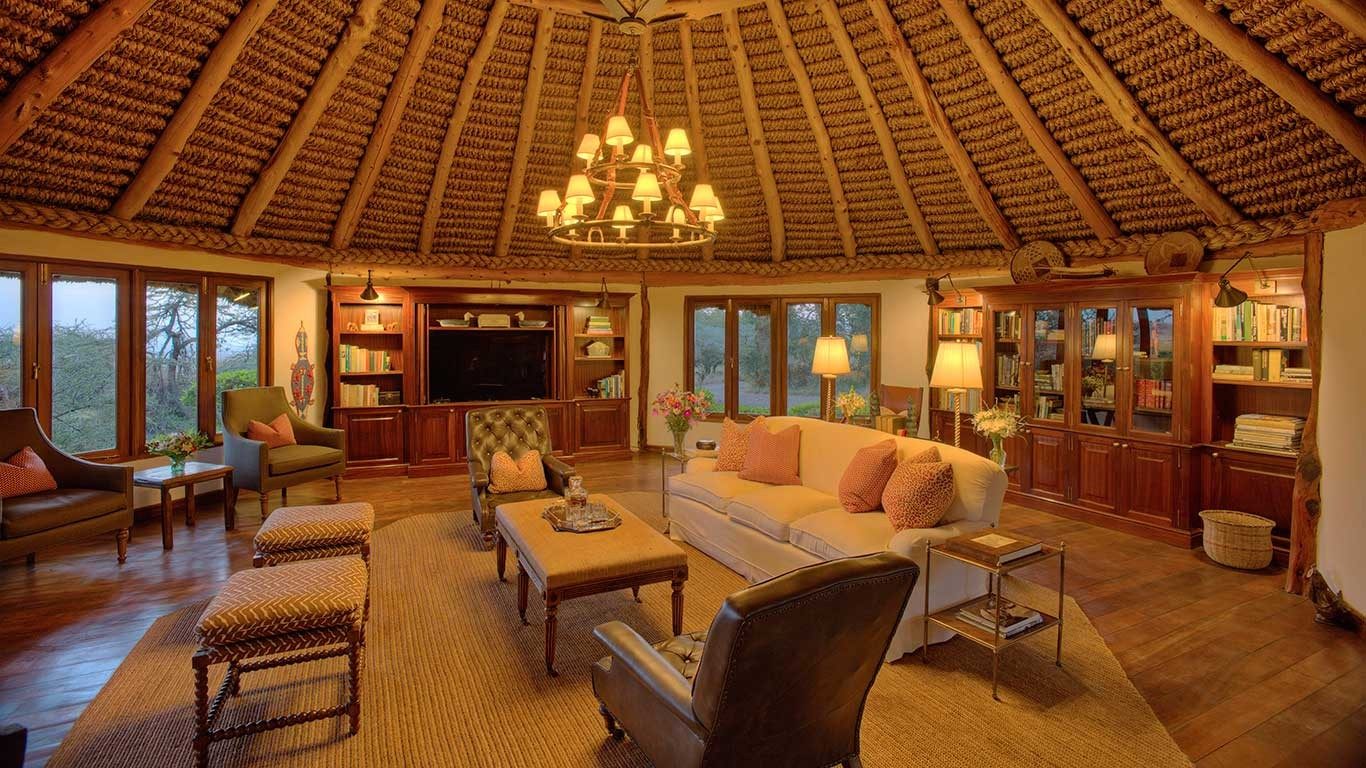 Round thatched lounge at Elewana Kifaru House with a chandelier, cream sofas, bookcases and windows on every side