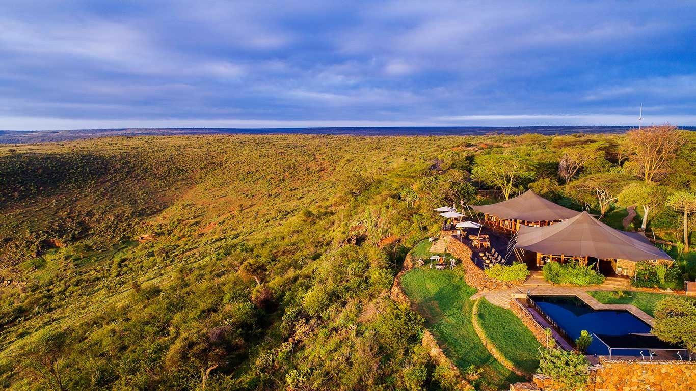 Aerial view of Elewana Loisaba Tented Camp on the edge of an escarpment, with its pool and tents above green plains