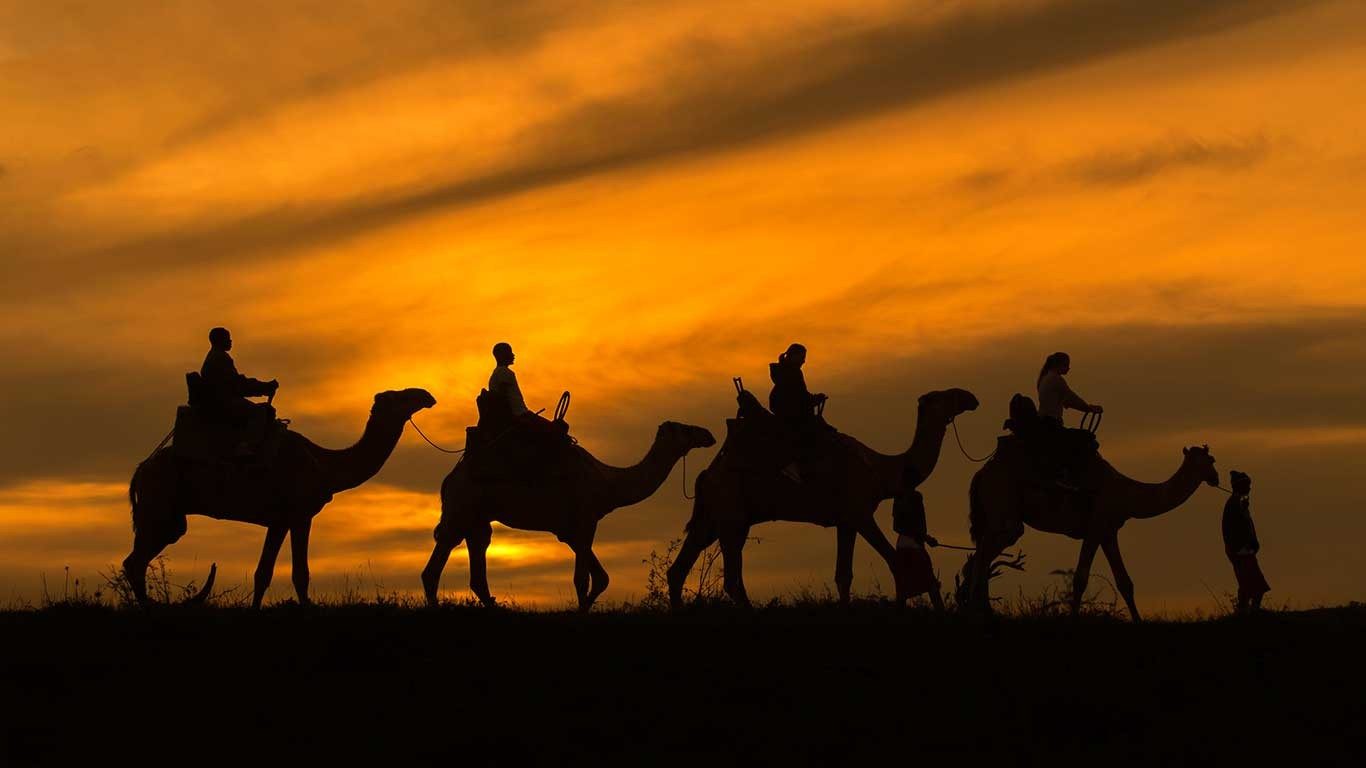 Camels and riders silhouetted against an orange sunset on a camel ride from Elewana Loisaba Tented Camp