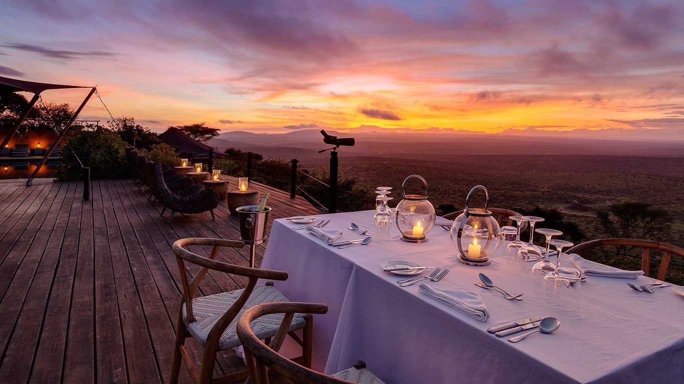 Dinner table laid with candles and glasses on the deck at Elewana Loisaba Tented Camp as the sun sets