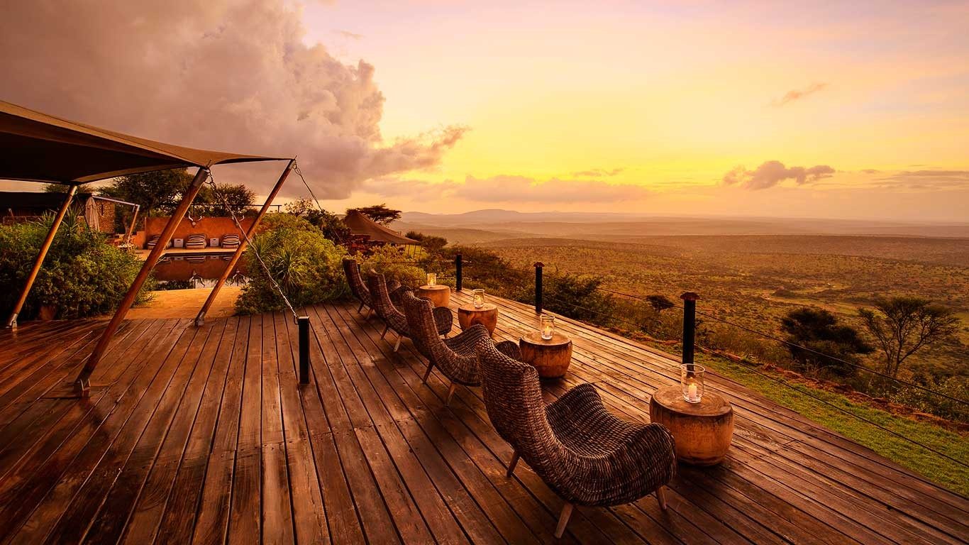 Long wooden deck with wicker chairs at Elewana Loisaba Tented Camp, looking over the plains under a glowing sunset