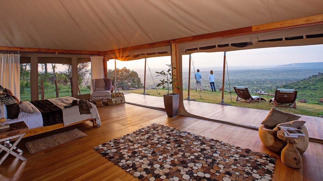 Tent at Elewana Loisaba Tented Camp with a wooden floor, a patterned rug and wide glass walls onto a deck and the valley