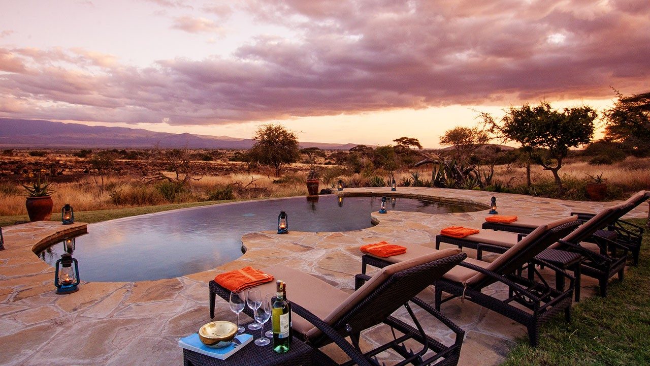 Swimming pool with loungers and orange cushions on a stone deck at Elewana Tortilis Camp Amboseli at sunset