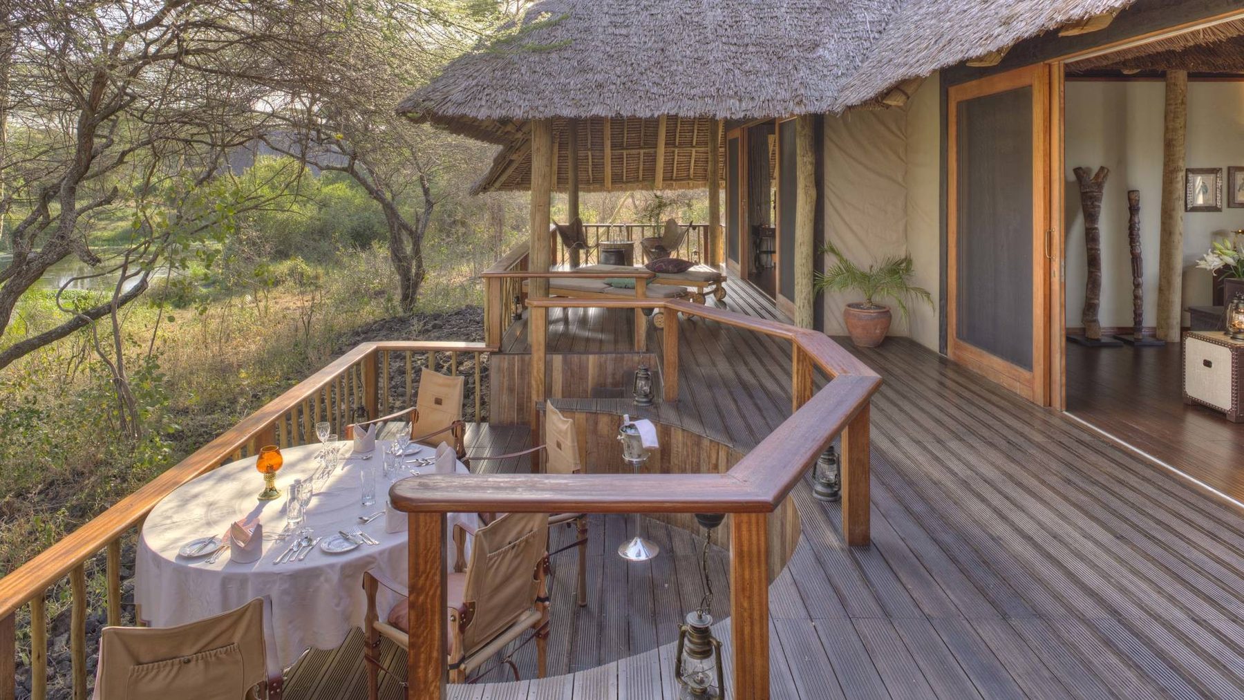 Wooden deck with a set dining table beside the thatched main building at Finch Hattons