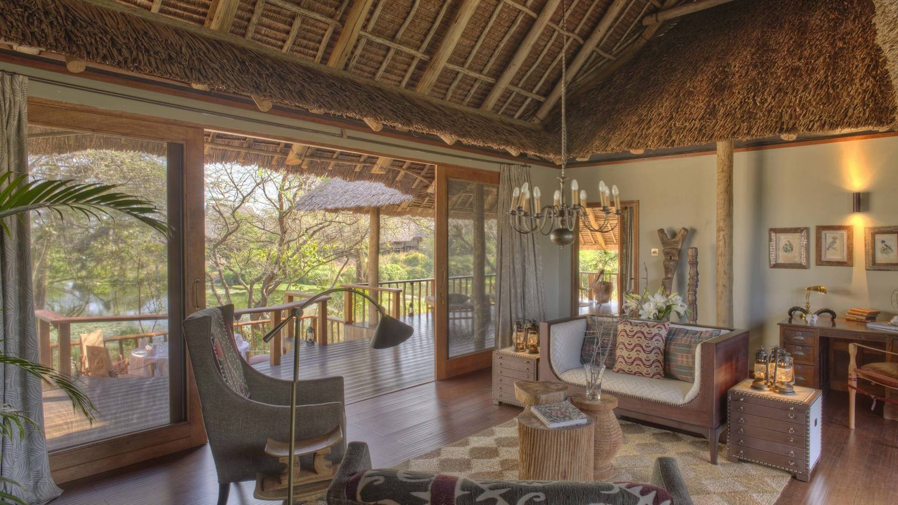 Main lounge at Finch Hattons with sofas, armchairs and chandeliers under a thatched roof, opening to the trees
