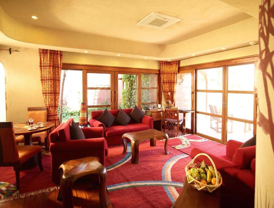 Lounge at Amboseli Serena Safari Lodge with red sofas, wooden tables and glass doors to a garden