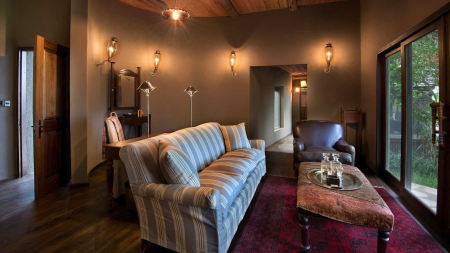 Sitting room at &Beyond Bateleur Camp with a striped sofa, leather armchair, wall lamps and a red rug