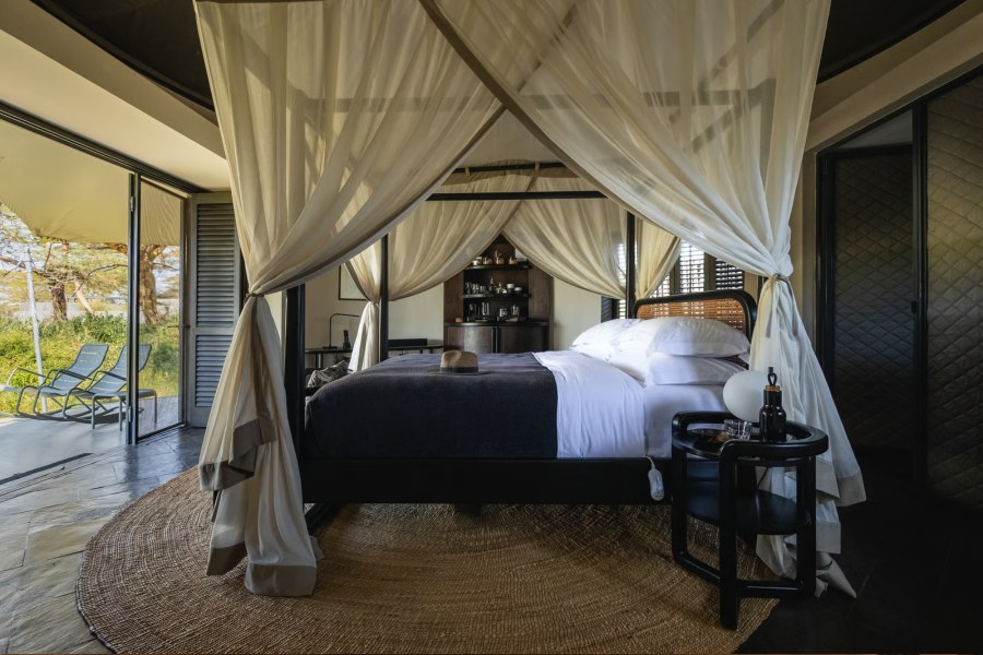 Suite at Angama Amboseli with a four-poster bed under white netting and doors open to a deck with loungers