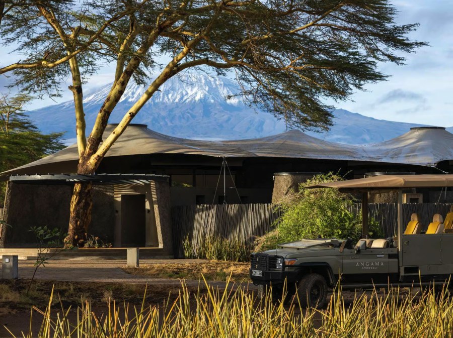 Main building at Angama Amboseli under a fever tree, with a game drive vehicle and Kilimanjaro behind