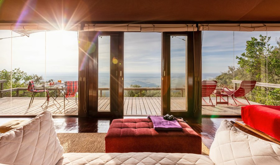 View from the bed in a suite at Angama Mara through glass doors to a deck and the valley below