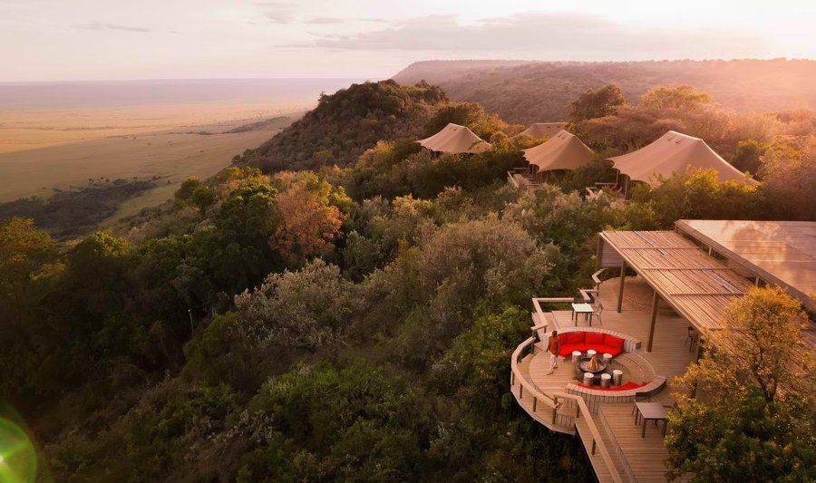 Tents and a deck with a red seating area on the wooded Oloololo Escarpment at Angama Mara, plains below