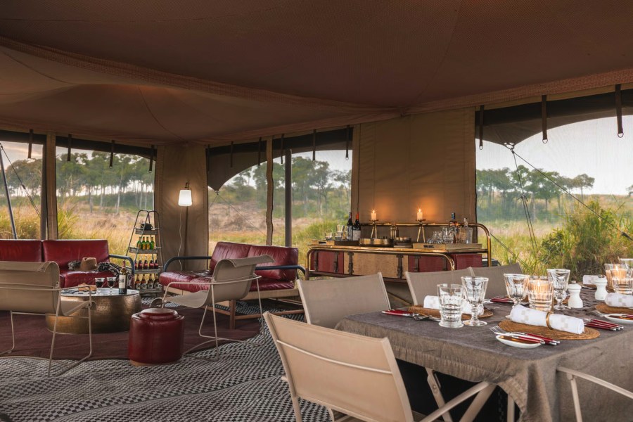 Mess tent at Angama Safari Camp with a laid dining table, red leather sofas and a bar with candles