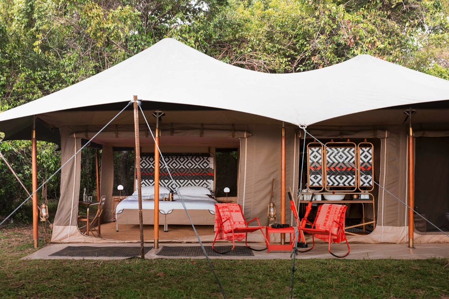 Canvas tent at Angama Safari Camp with a patterned headboard, a washstand and red chairs out front