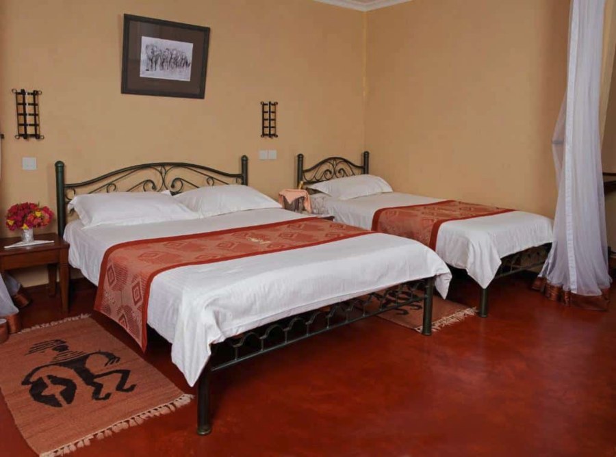 Room at Ashnil Aruba Lodge with two beds with iron frames, a framed elephant print and a red floor