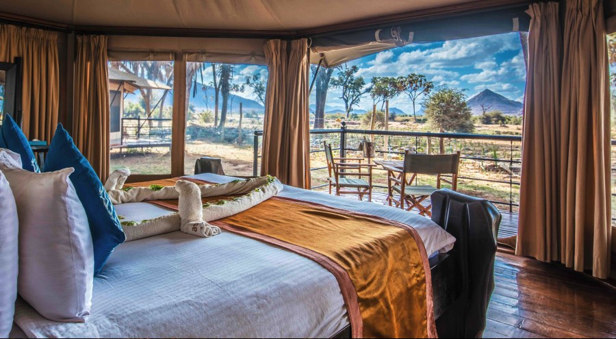 Tent at Ashnil Samburu Camp with a bed and a deck looking out to doum palms and a pointed hill