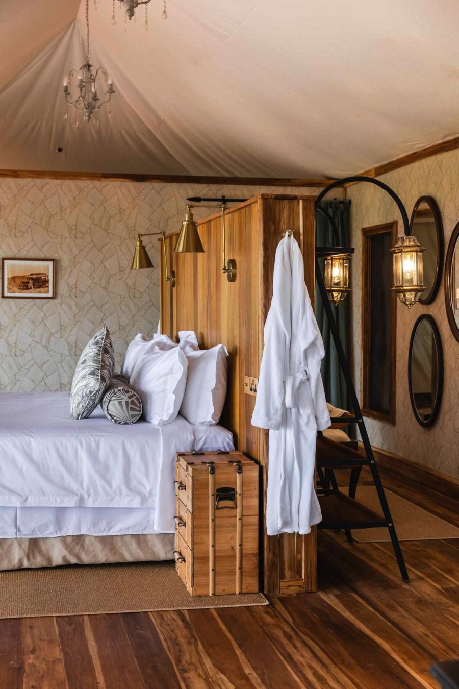 Tent at Cottar’s 1920s Camp with a white bed, a wooden trunk, a hanging robe and a chandelier