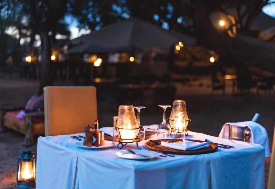 Dinner table for two set with candle lanterns and wine glasses outdoors at Elephant Bedroom Camp