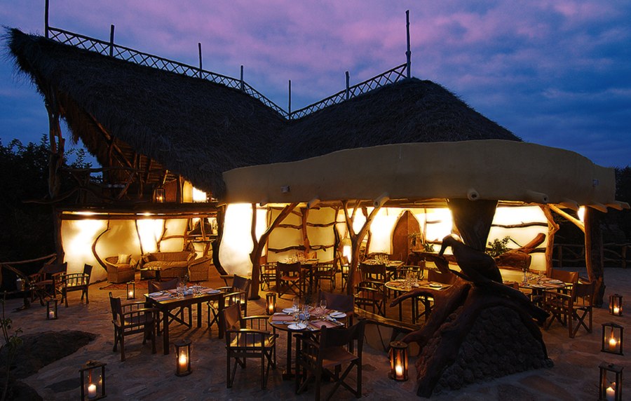 Outdoor dining terrace at Satao Elerai at dusk, lit by lanterns under a tall thatched roof